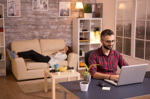 handsome-man-working-laptop-living-room-girlfriend-relaxing-sofa-talking-her-phone-chips-table