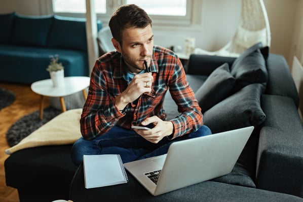 thoughtful-man-using-mobile-phone-laptop-while-working-home